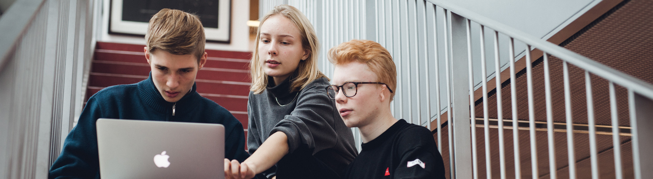 Tre elever sidder på hovedtrappen og kigger på computerskærm.