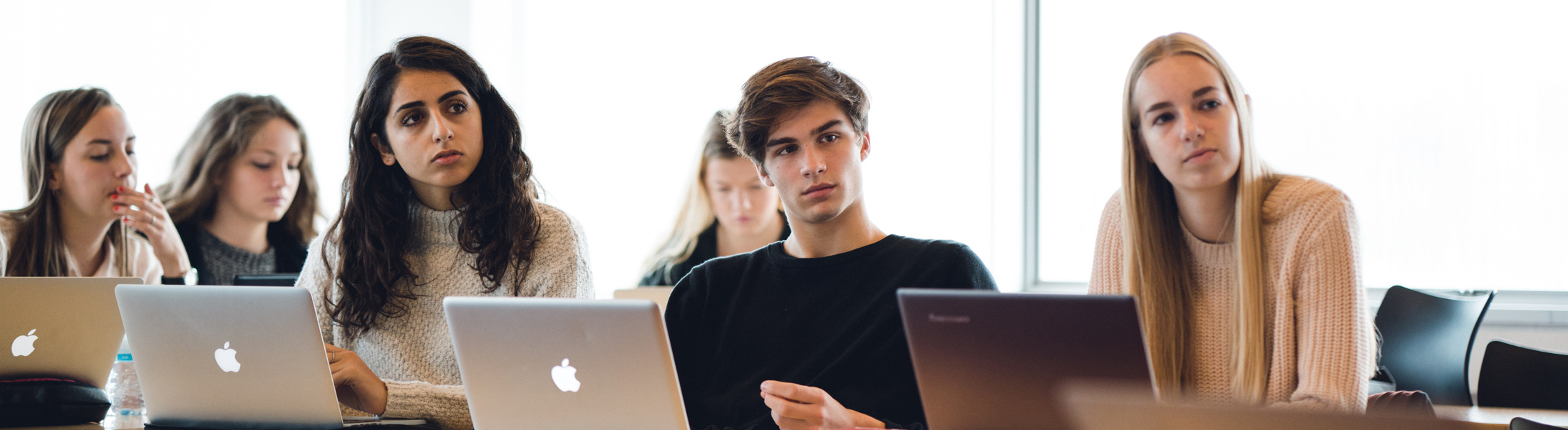 Elever med laptops sidder og kigger op mod tavle.
