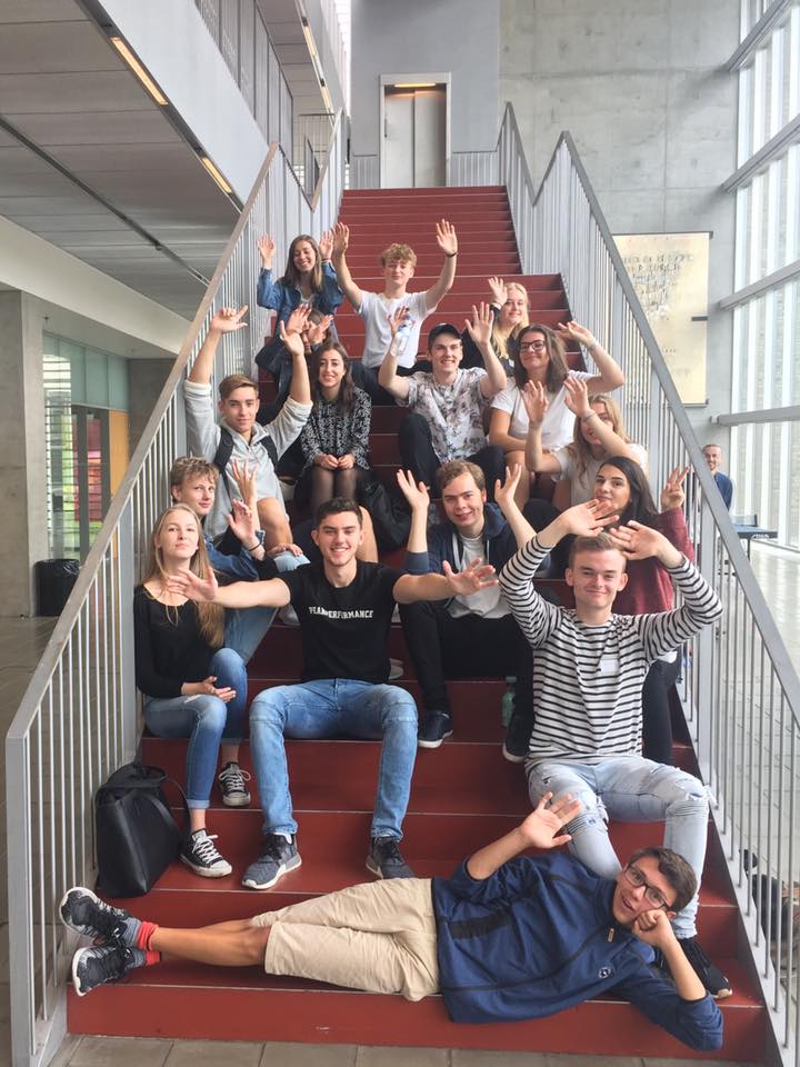 Foto af 16 tutorer der sidder på hovedtrappen i forhallen og byder velkommen.