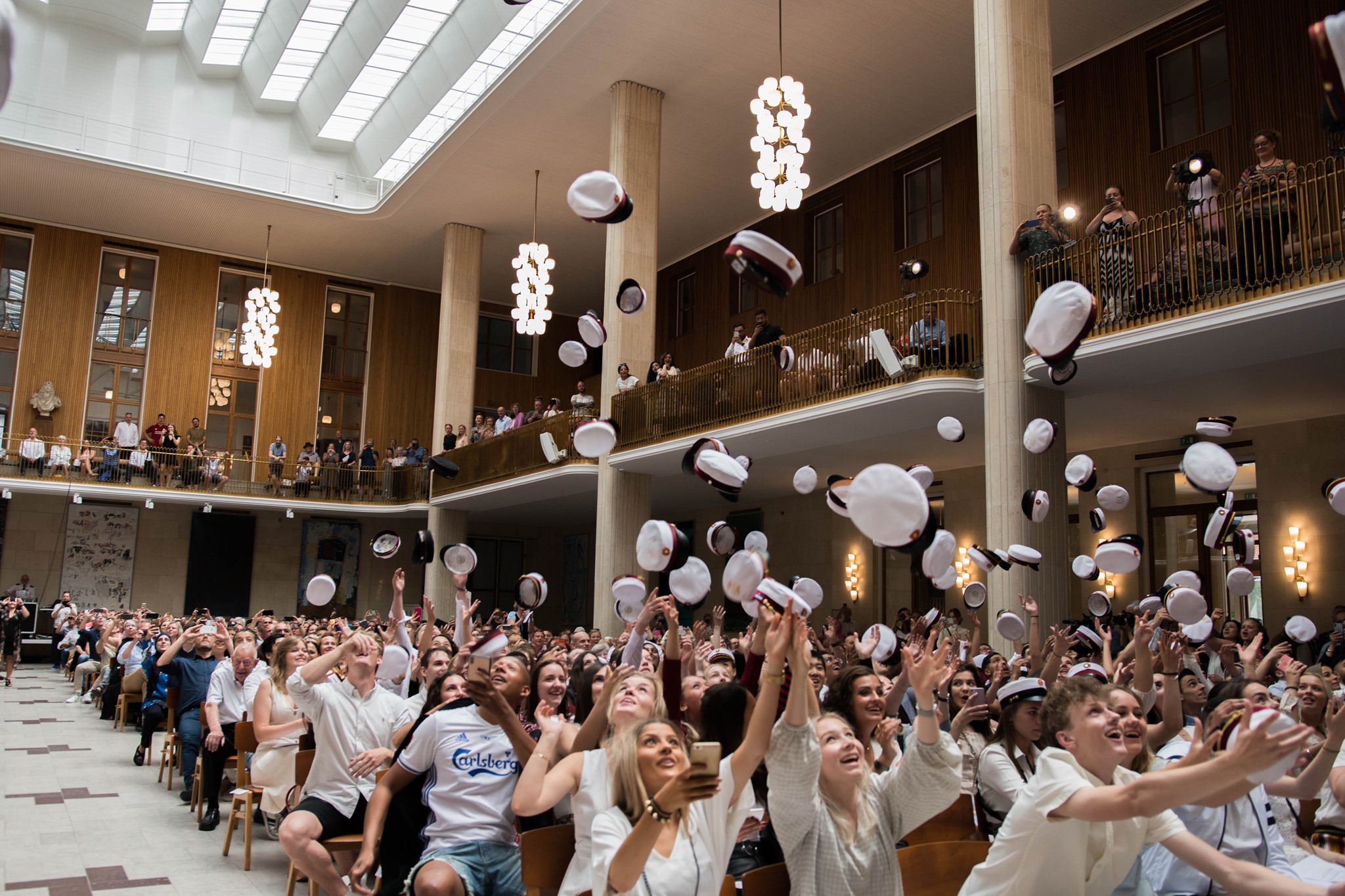 Foto af studenterne i Frederiksberg Rådhus festsal til translokation. De kaster studenterhuerne op i luften.